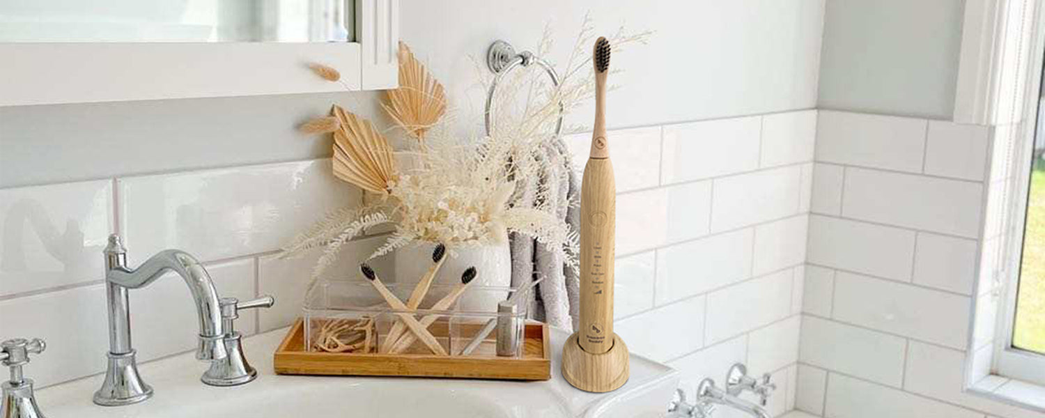 Bathroom corner with a Bamboo Buddy electric bamboo toothbrush, charging station, Bamboo Buddy Adult toothbrushes, Bamboo Buddy Floss Picks, Bamboo Buddy Tongue Cleaner, and Bamboo Buddy Eco Floss Dispenser.