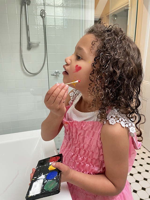 Child applying makeup or face paint with a cotton tip in a bathroom setting