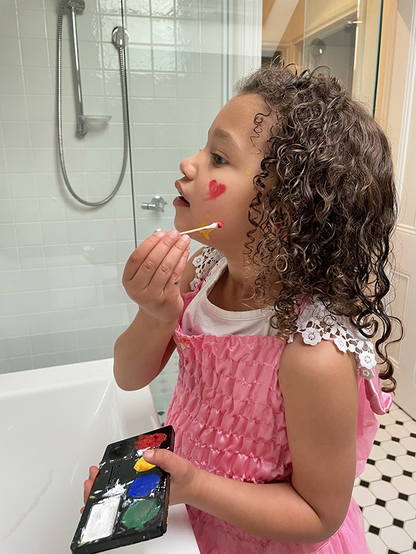 Child applying makeup or face paint with a cotton tip in a bathroom setting